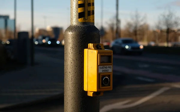 Přechodové tlačítko pro pěší se světelným varováním. Rozostřené pozadí s vozy řídit po silnici a bokeh od reflektorů. Nápis v češtině - Tlacitko pro chodce- Tlačítko pro chodce. — Stock fotografie