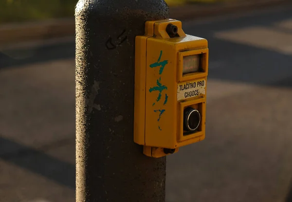 Přechodové tlačítko pro pěší se světelným varováním. Rozostřené pozadí s vozy řídit po silnici a bokeh od reflektorů. Nápis v češtině - Tlacitko pro chodce- Tlačítko pro chodce. — Stock fotografie