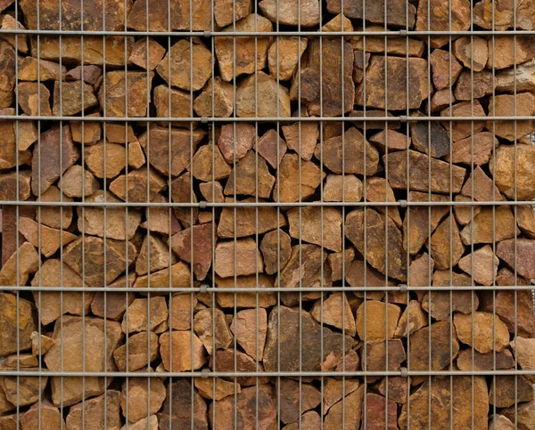 Gabion retaining wall - close-up brown stones in gabion metallic baskets kept by retaining wall. Gabions protective wall filled with stones and tied with thick metal wire. Eco wall textured design.