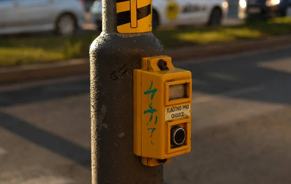 Přechodové tlačítko pro pěší se světelným varováním. Rozostřené pozadí s vozy řídit po silnici a bokeh od reflektorů. Nápis v češtině - Tlacitko pro chodce- Tlačítko pro chodce. — Stock fotografie