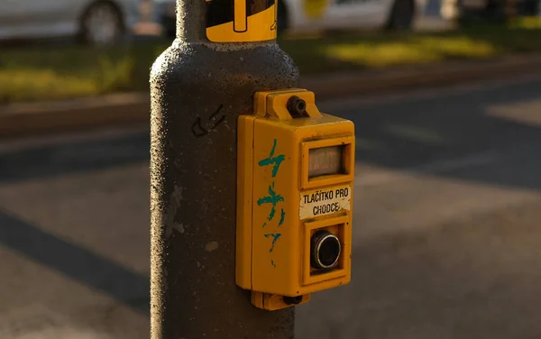 Tombol Crosswalk untuk pejalan kaki dengan peringatan cahaya. Latar belakang yang tidak fokus dengan mobil mengemudi di sepanjang jalan dan bokeh dari lampu depan. Prasasti di Ceko-Tlacitko pro chodce- Tombol untuk pejalan kaki. — Stok Foto