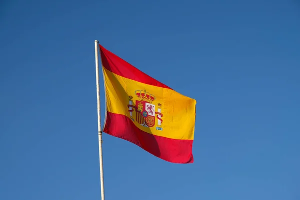 Bandiera nazionale spagnola sventola su sfondo cielo blu. La bandiera su un pennone sventola nel vento. Rosso con giallo Spagna Bandiera che soffia nel vento contro sul cielo blu — Foto Stock