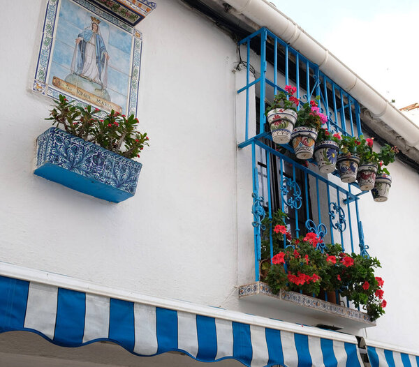 Typical decorated facade of white wall house, blue windows and balconies with flowering plants in clay pots - geranium, pelargonium in province of Malaga, Andalusia, Spain. Houseplants in pots,outdoor