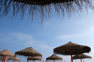 Malaga, Endülüs, İspanya 'daki tipik saman plajı şemsiyesi. Arka arkaya saman plaj şemsiyeleri, Akdeniz kıyısı, kumlu plaj. Bulutlu bir gün, denizde sis