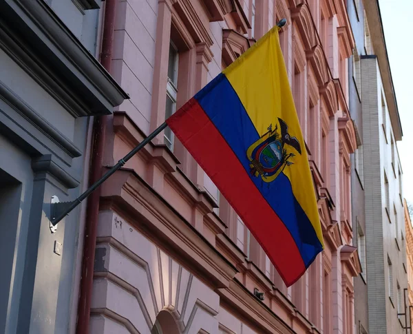 Bandera nacional de Ecuador, tricolor de amarillo, azul y rojo, escudo de armas con Cóndor. Bandera de Ecuador sobre asta de bandera ondea contra edificio de Embajada de Ecuador en Praga, República Checa. Imagen de stock