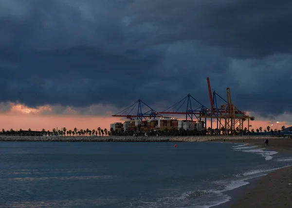 Farbenfroher Sonnenuntergang über dem Seehafen und Industriekränen. Strandlinie mit Blick auf den Hafen von Spanien. Transport und logistischer Hintergrund - Seecontainer werden von Schiffen mit riesigen Kränen abtransportiert — Stockfoto