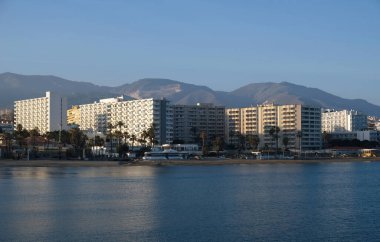 Malaga, Endülüs, İspanya 'daki Akdeniz kıyısındaki yüksek binalar ve otellerin manzarası. Kumsal manzarası, palmiye ağaçları, mavi deniz, mavi gökyüzü ve dağlar. Emlak kavramı.