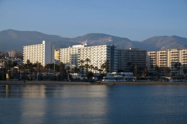 Malaga, Endülüs, İspanya 'daki Akdeniz kıyısındaki yüksek binalar ve otellerin manzarası. Kumsal manzarası, palmiye ağaçları, mavi deniz, mavi gökyüzü ve dağlar. Emlak kavramı.