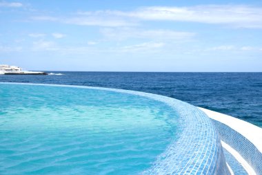 Deniz manzaralı bir tatil köyünde yüzme havuzunda mavi berrak su yüzeyi. Yaz tatili ve dinlenme konsepti. Lüks yazlık villa evi. Mavi karo mozaik deseni.
