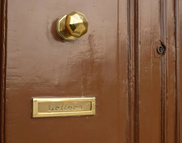 Brown vintage door with gold door handle, mailbox slot in the door with vintage lettering.