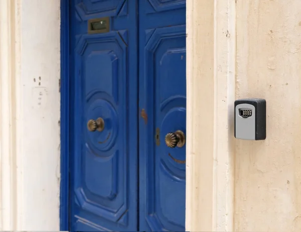 Smart key lock mounted on wall for renting apartment. Safe Key Box is used when the guest arrives at the touristic flat and the host can't open the door. Safe access to living space. Blue vintage door