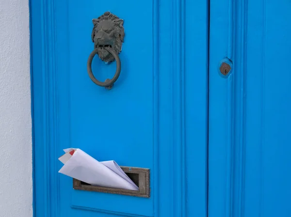 Blue vintage door with a knocker in the shape of a lion, mailbox slot in the door with advertising newspapers.