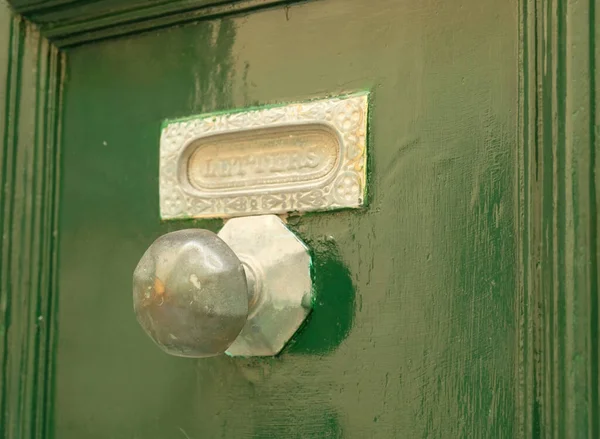 Green vintage door with silver door handle, mailbox slot in the door with vintage lettering.
