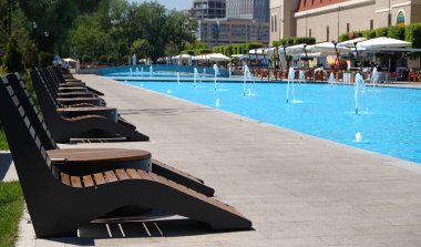 A recreation and relaxation area by the pool in a hotel or a fountain in a park. Row of water jets in a modern fountain, blue water. Streams flowing out of the tube. Summer cityscape. 