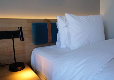 Close-up fragment of bedroom with empty bedside table, turn on reading lamp and a socket in modern interior design home or hotel. Soft pillow and blanket, stylish comfortable furniture.