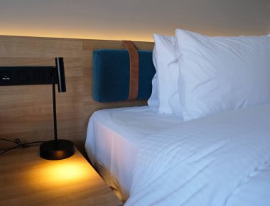 Close-up fragment of bedroom with empty bedside table, turn on reading lamp and a socket in modern interior design home or hotel. Soft pillow and blanket, stylish comfortable furniture.