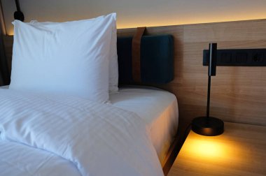 Close-up fragment of bedroom with empty bedside table, turn on reading lamp and a socket in modern interior design home or hotel. Soft pillow and blanket, stylish comfortable furniture.