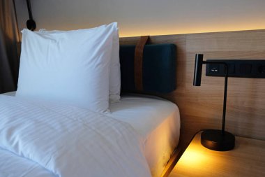 Close-up fragment of bedroom with empty bedside table, turn on reading lamp and a socket in modern interior design home or hotel. Soft pillow and blanket, stylish comfortable furniture.