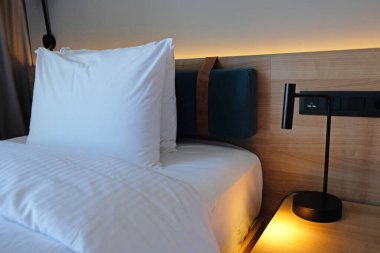 Close-up fragment of bedroom with empty bedside table, turn on reading lamp and a socket in modern interior design home or hotel. Soft pillow and blanket, stylish comfortable furniture.