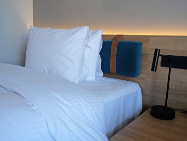 Close-up fragment of bedroom with empty bedside table, turn off reading lamp and a socket in modern interior design home or hotel. Soft pillow and blanket, stylish comfortable furniture.