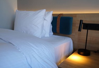 Close-up fragment of bedroom with empty bedside table, turn on reading lamp and a socket in modern interior design home or hotel. Soft pillow and blanket, stylish comfortable furniture.