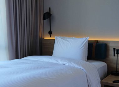 Close-up fragment of bedroom with empty bedside table, turn off reading lamp and a socket in modern interior design home or hotel. Soft pillow and blanket, stylish comfortable furniture.