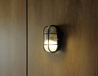Turned on yellow light Industrial style metal black wall lamp. Wall hanging lamp on a brown wooden wall, night light. Industrial style decor in interior. Minimalism.