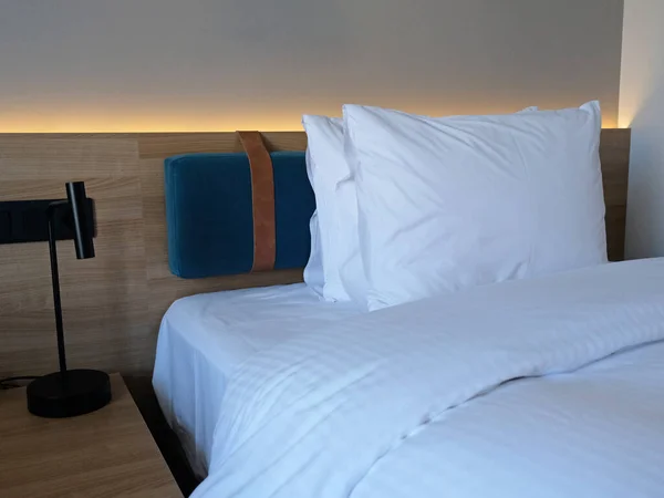 Close-up fragment of bedroom with empty bedside table, turn off reading lamp and a socket in modern interior design home or hotel. Soft pillow and blanket, stylish comfortable furniture.