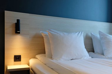 Close-up fragment of bedroom with empty bedside table, turn on reading lamp and a socket in modern interior design home or hotel. Soft pillow and blanket, stylish comfortable furniture.