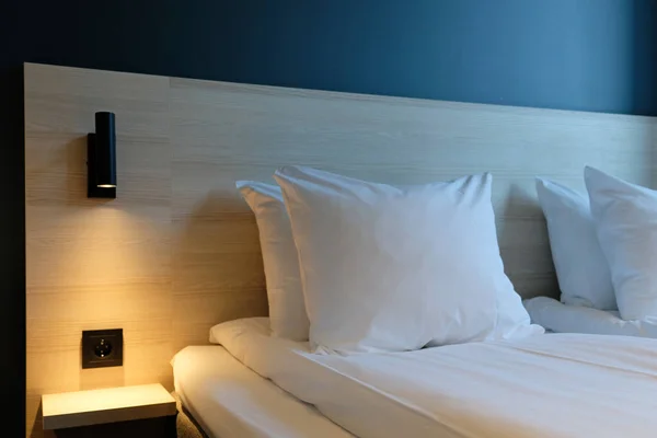 Close-up fragment of bedroom with empty bedside table, turn on reading lamp and a socket in modern interior design home or hotel. Soft pillow and blanket, stylish comfortable furniture.