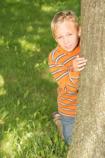 Jongen op zoek achter een boom — Stockfoto