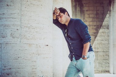 Genç bunalımlı ve yorgun bir adam beyaz bir duvara yaslanmış. Günlük kıyafet..