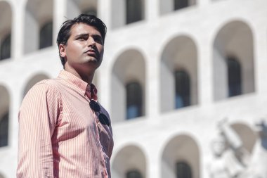 Bir binanın önünde duran bir iş adamı. Tişört giyiyordu. Mesafeye bak..