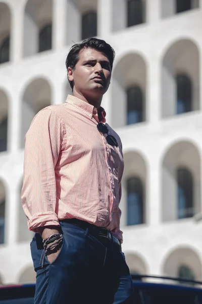 Business man standing in front of a building. Wearing a shirt and formal suit. Hands in the pocket.