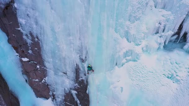Людина-альпініст веде на лід. Льодовик впадає на замерзлий водоспад. Повітряний вид — стокове відео
