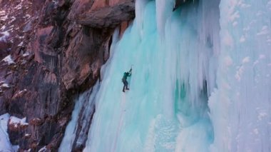 Mountaineer Man is leading on Ice. Ice Climbing on Frozen Waterfall, Aerial View. Barskoon Valley, Kyrgyzstan. Drone Flies Upwards, Tilt Down. Crane Shot