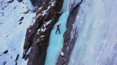 Ice Climbing on Frozen Waterfall. Mountaineer Woman is leading on Ice. Aerial Top-Down View. Barskoon Valley, Kyrgyzstan. Drone Flies Downwards, Tilt Up. Crane Shot