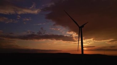 Gün batımında tarlada yel değirmeni türbini silueti. Dönen rüzgar jeneratörü