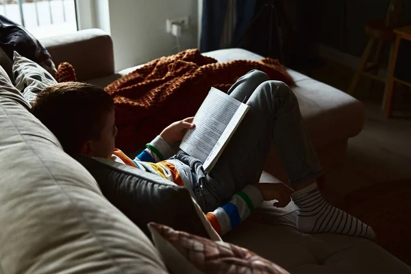 Dziecko chłopiec czyta książkę na kanapie w domu — Zdjęcie stockowe