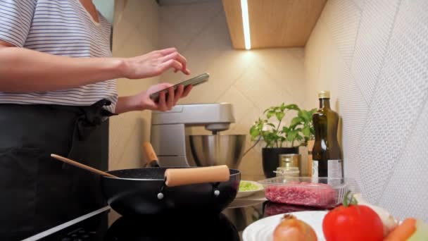 Frau kocht Sauce Bolognese und nutzt Smartphone — Stockvideo