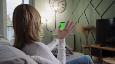 Oturma odasındaki kadın video görüşmesi için akıllı telefon kullanıyor.