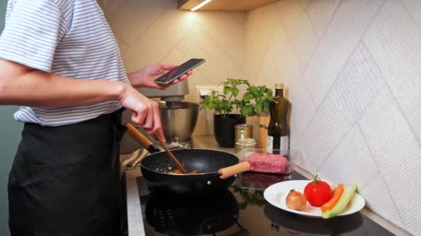 Kvinna matlagning sås bolognese och använda smartphone — Stockvideo