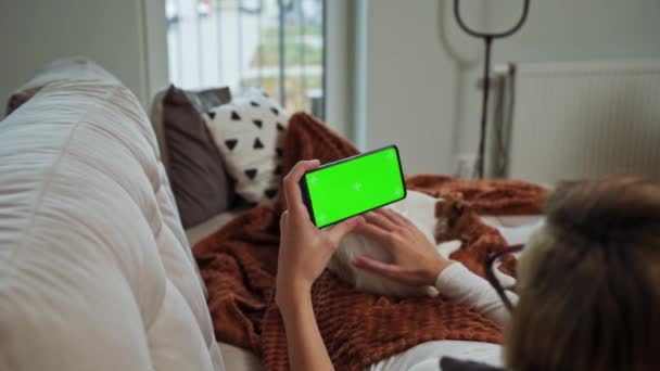 Женщина лежит на диване и смотрит онлайн видео на смартфоне с хрома-ключом — стоковое видео
