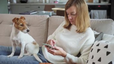 Kadın köpekle oturur ve akıllı telefon kullanır.