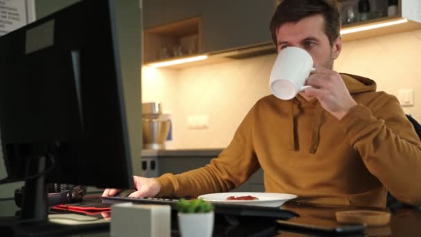 El hombre trabaja remotamente en la oficina del hogar y bebe café — Vídeo de stock