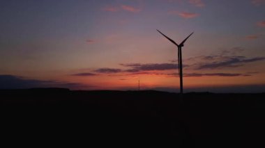 Gün batımında tarlada yel değirmeni türbini silueti. Dönen rüzgar jeneratörü