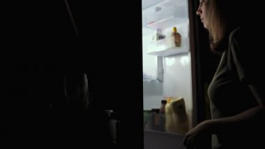 Kadın geceleri buzdolabından elma alıyor.