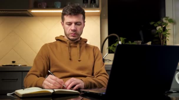 Ο άνθρωπος εργάζεται χρησιμοποιώντας φορητό υπολογιστή στο χώρο εργασίας στο σπίτι, διαβάζοντας έγγραφα χαρτί — Αρχείο Βίντεο