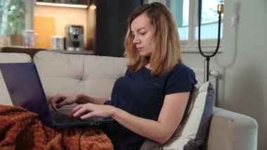 Serbest çalışan kadın kanepede uzanıyor ve çalışmak için dizüstü bilgisayar kullanıyor. Ev işi, uzaktan çalışma.