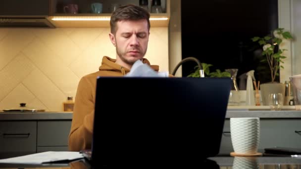 Чоловік працює з ноутбуком на домашньому робочому місці, читаючи паперові документи — стокове відео